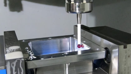 A machined aluminum part in a machine vice with a spindle probe tip contacting an inner surface of the part.