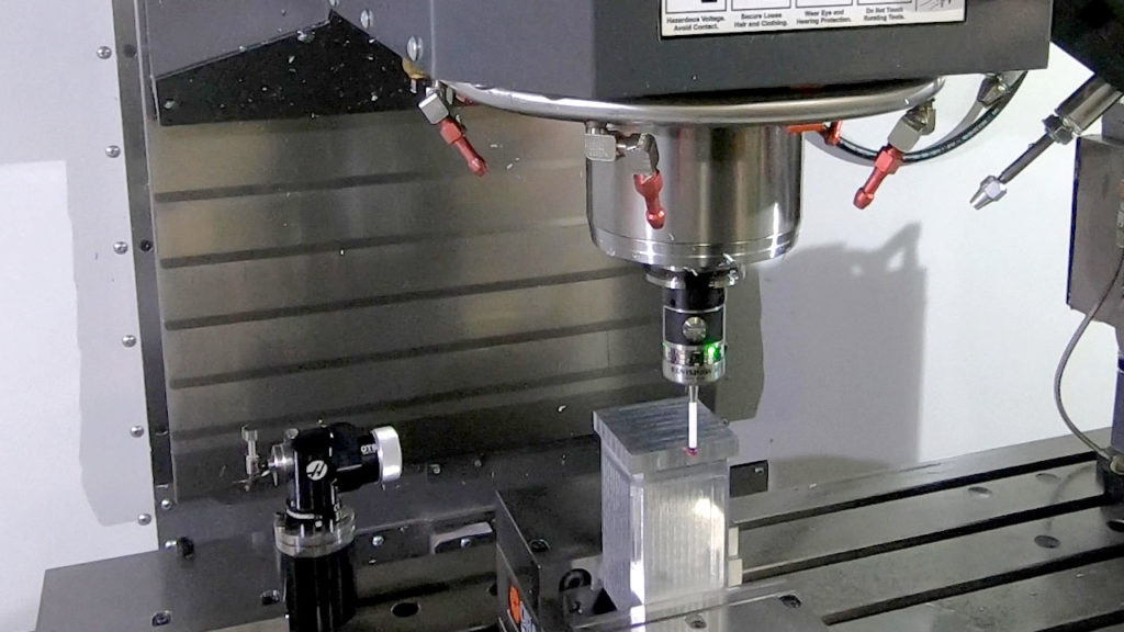 Probe inspecting rectangular part in CNC machine.
