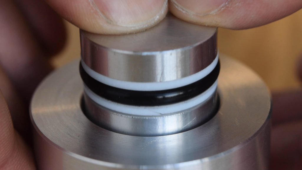 Zoomed-in view of fingers pushing a piston with O-rings and backup rings into another component.