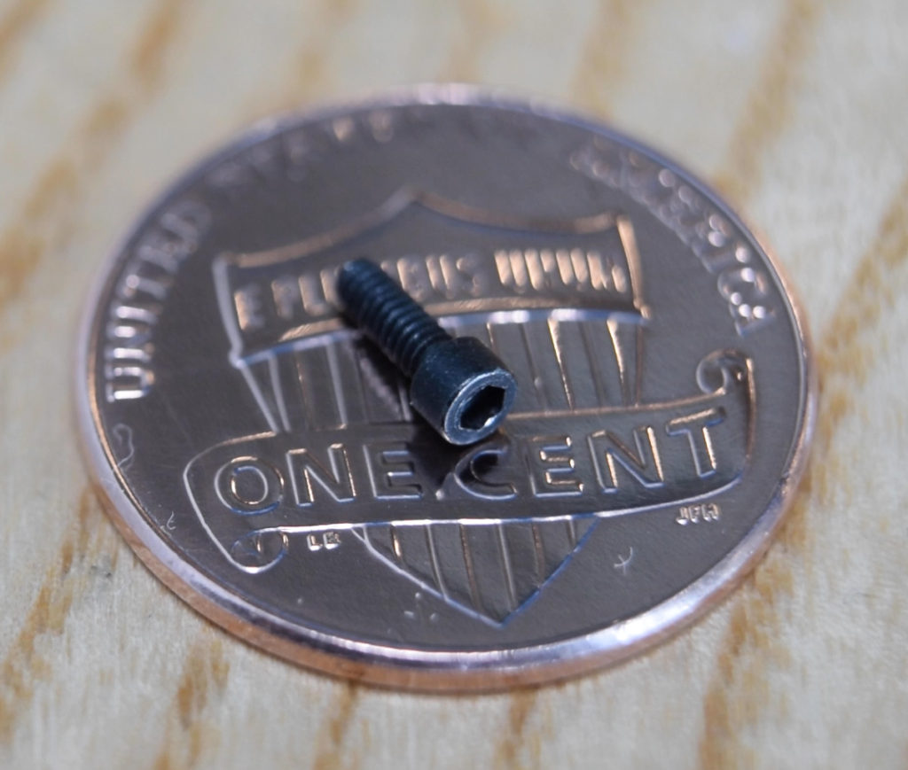 a 0-80 microscrew sitting on a penny for scale. The screw is approximately 1/5 the width of the penny.