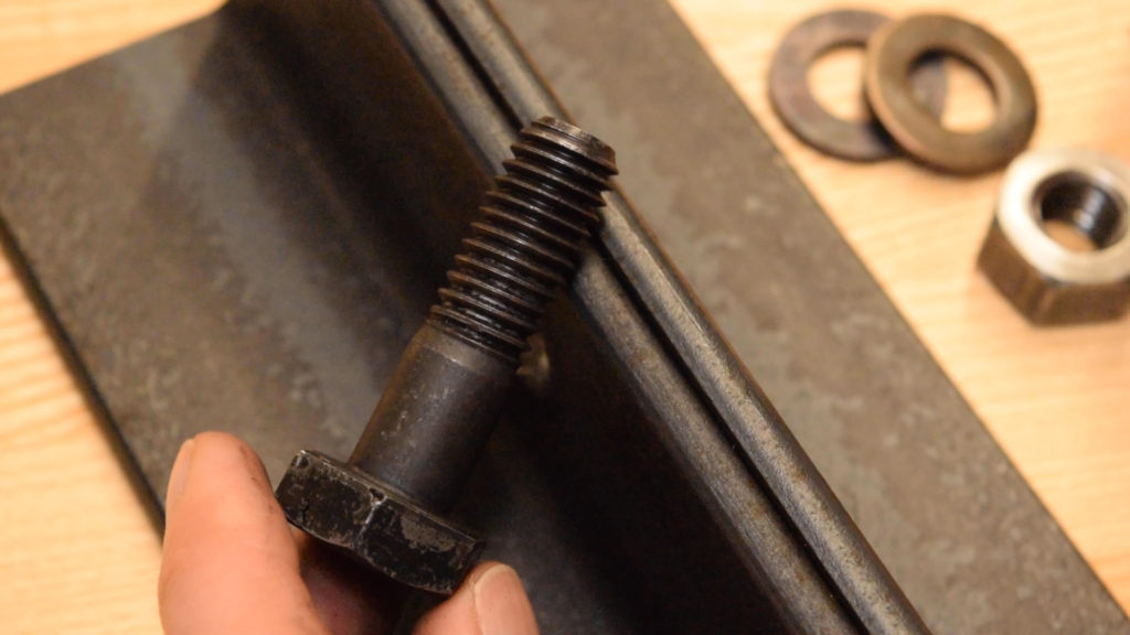 A structural bolt next to some structural steel demonstrating that the unthreaded section is meant to carry shear loads.