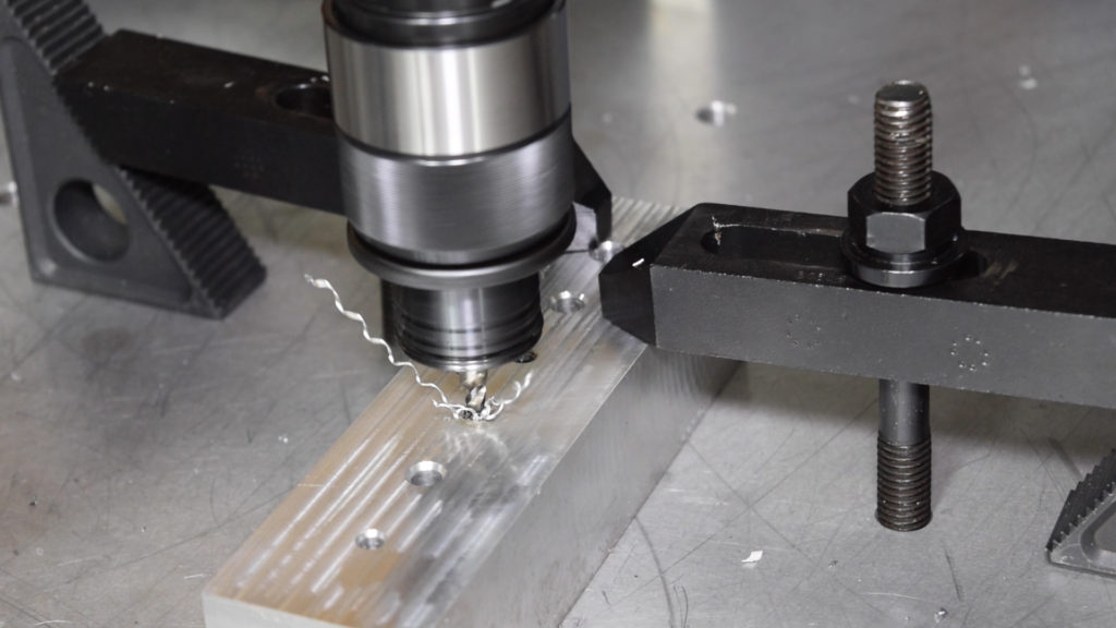 A powered tapping head cutting threads into an aluminum workpiece